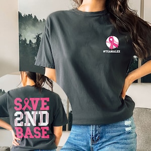 May include: Black t-shirt with a pink ribbon and baseball graphic on the front and the text "SAVE 2ND BASE" in pink on the back. The text "#TEAMALEX" is printed below the graphic on the front.