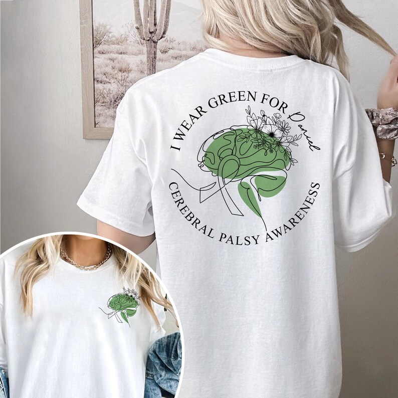 May include: White t-shirt with a green brain graphic and the text "I wear green for Daniel Cerebral Palsy Awareness". The design includes a green brain with floral accents. The shirt is a casual wear item.