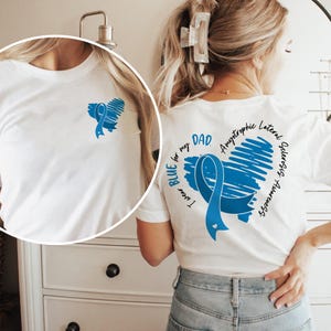 May include: White t-shirt with a blue ribbon heart design on the back. The text on the shirt reads "I wear BLUE for my DAD. Amyotrophic Lateral Sclerosis Awareness".
