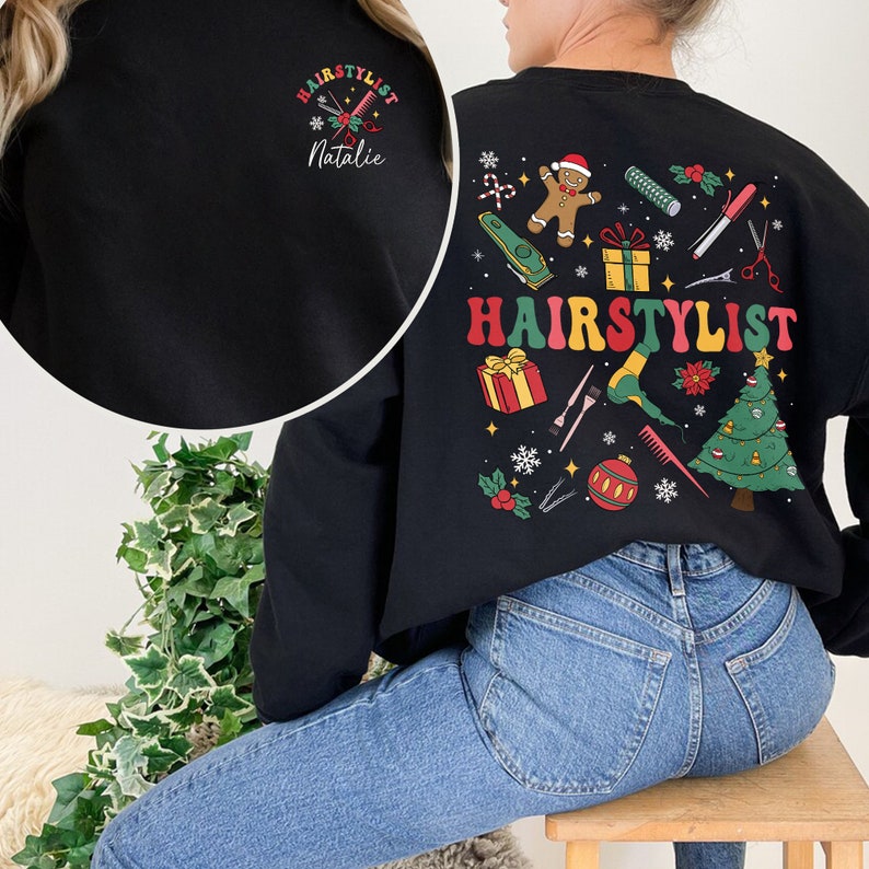 Op de afbeelding: Zwart sweatshirt met een kerstthema ontwerp met een peperkoekman, een kerstboom en de tekst "HAIRSTYLIST". Het sweatshirt heeft ook een kleiner ontwerp aan de voorkant met de tekst "HAIRSTYLIST Natalie".