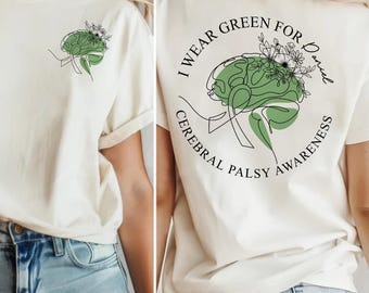 Può includere: T-shirt color crema con grafica di un cervello verde e la scritta "I Wear Green For Daniel Cerebral Palsy Awareness". La parte anteriore della maglietta presenta una grafica del cervello più piccola. Il design include accenti floreali.