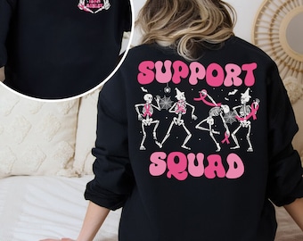 May include: Black sweatshirt with a pink and white graphic of skeletons dancing with pink ribbons. The text "SUPPORT SQUAD" is in pink letters.