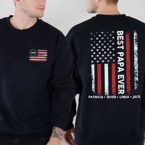 Puede incluir: Sudadera negra con un dise&ntilde;o de bandera estadounidense desgastada en la espalda. El texto "Best Papa Ever" est&aacute; impreso verticalmente en la bandera. Los nombres "Patricia, River, Linda, Jack" est&aacute;n impresos debajo de la bandera. Una bandera estadounidense m&aacute;s peque&ntilde;a con la palabra "Papa" est&aacute; impresa en la parte delantera de la sudadera.