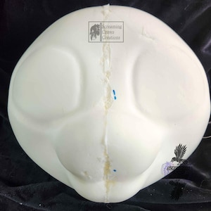 May include: A white foam head base with large eye sockets and a rounded shape. The head base has a seam running down the center and is likely for a costume or art project. The text "Screaming Crows Creations" is visible.