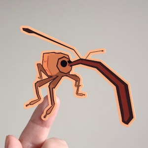 May include: A brown and orange insect sticker with a long, curved snout. The insect has six legs and is in a walking position. The sticker is on a finger.