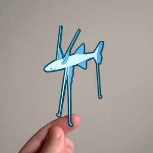 Könnte beinhalten: Ein blauer und weißer Papier-Ausschnitt eines Fisches mit langen, dünnen Beinen. Der Fisch steht auf einem Finger.