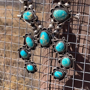 Puede incluir: Un collar nativo americano de turquesa y plata con múltiples piedras turquesa engastadas en plata. El collar está colgado de una valla de alambre.