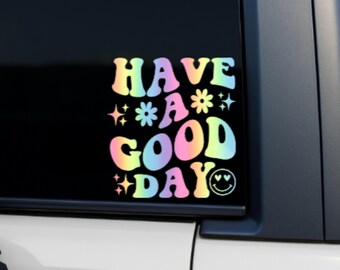 May include: A colorful sticker with the words "HAVE A GOOD DAY" in a retro font. The text is in rainbow colors with stars, flowers, and a smiling face. The sticker is on a black surface.