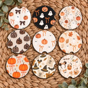 Könnte beinhalten: Neun runde Auto-Untersetzer mit verschiedenen Halloween-Motiven, darunter orangefarbene Kürbisse, weiße Geister, braune Schleifen, Kürbisse mit Leopardenmuster, Herbstblätter, Hexenhüte und Mausohr-Haarreifen auf cremefarbenen, schwarzen und weißen Hintergründen.