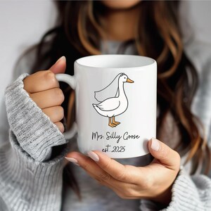 Puede incluir: Taza de cer&aacute;mica blanca con una ilustraci&oacute;n de dibujos animados de un ganso con velo. El texto en la taza dice "Mrs. Silly Goose est. 2025".