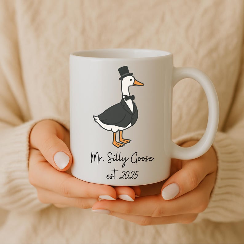 Puede incluir: Taza de cer&aacute;mica blanca con una ilustraci&oacute;n de dibujos animados de un ganso con un sombrero de copa y esmoquin. El texto "Mr. Silly Goose est. 2025" est&aacute; impreso debajo del ganso.