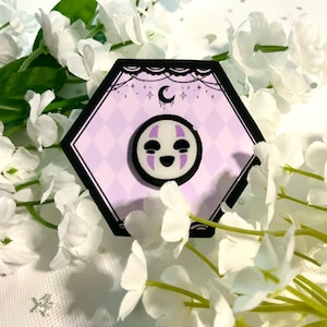 May include: A white and purple No Face character from the movie Spirited Away is featured on a round pin. The pin is on a hexagonal card with a black border and a purple background. The card has a crescent moon and stars on it.