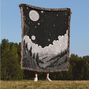 May include: Black and white woven tapestry featuring a mountain landscape with a full moon and stars in the night sky.