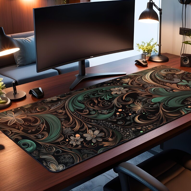 May include: A black, green, and gold patterned desk mat with a floral design. The mat is on a wooden desk with a computer monitor, a lamp, and a plant.