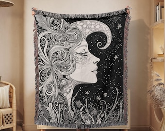 May include: Black and white woven throw blanket with a detailed illustration of a woman's face with intricate hair and a crescent moon behind her. The background is a black starry night.
