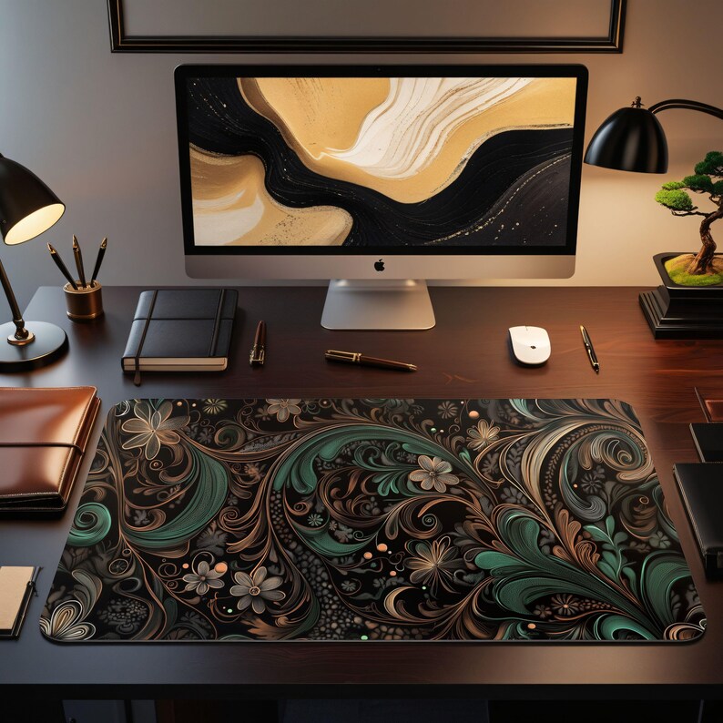 May include: A black desk mat with a green and gold floral pattern. The mat is on a wooden desk with a computer, a lamp, and other office supplies.