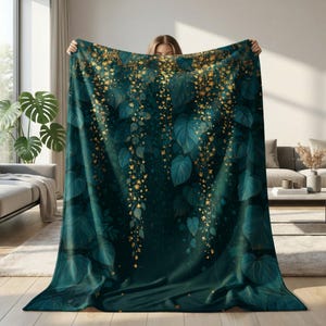 Puede incluir: Una manta rectangular con un fondo verde azulado oscuro y un patrón repetitivo de hojas grandes de color verde intenso y enredaderas florales doradas en cascada. El diseño crea un efecto botánico denso y superpuesto en la tela.