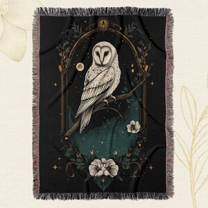 May include: A black tapestry with a white owl perched on a branch with flowers and a moon in the background. The owl is surrounded by a gold frame with a star design.