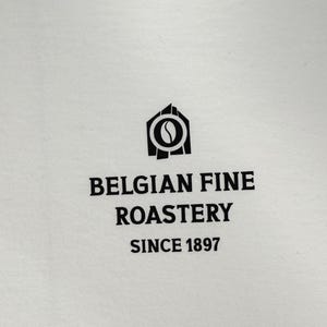 Op de afbeelding: Wit T-shirt met een zwart logo met de tekst "Belgian Fine Roastery Since 1897". Het logo toont een gestileerde koffieboon in een huis.