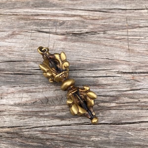 May include: A gold-colored metal Tibetan prayer wheel pendant with intricate details. The wheel is adorned with a decorative design and has a loop at the top for hanging.
