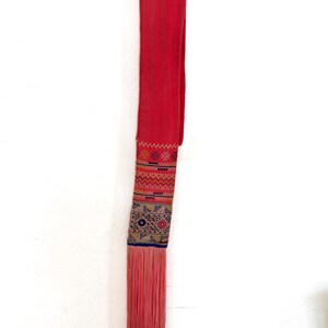 K&ouml;nnte beinhalten: Ein langer, roter Stoffscharf mit einer Franse am unteren Ende. Der Scharf hat ein buntes Stickmuster in der Mitte.