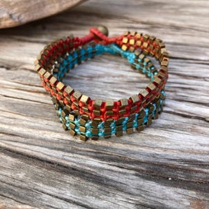 May include: A woven bracelet with red and blue threads and gold-toned metal beads.