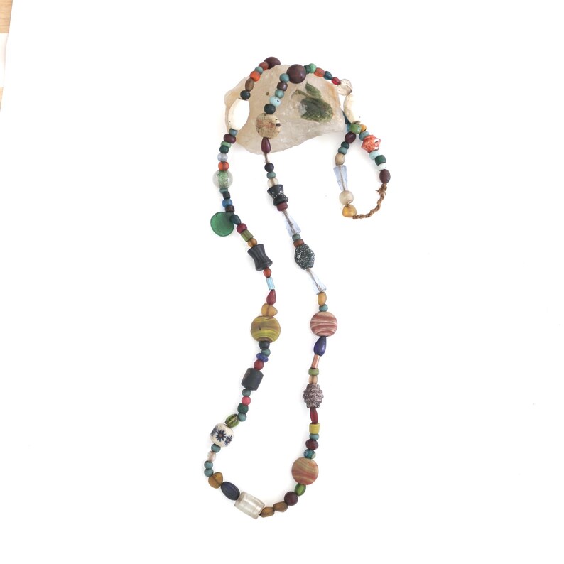 May include: A long, colourful necklace made of various beads, including glass, wood, and metal. The beads are in shades of blue, green, brown, red, and white.
