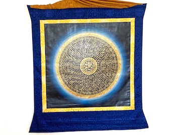 Puede incluir: Un tapiz rectangular con un diseño circular central con intrincada escritura dorada sobre un fondo oscuro. El diseño está enmarcado por un borde dorado y una tela azul estampada. La parte superior es de tela dorada.