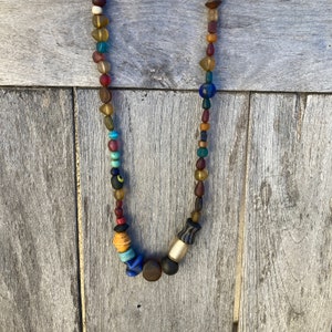 May include: A colourful beaded necklace with a variety of glass and wooden beads. The necklace features a mix of blue, red, brown, and yellow beads.