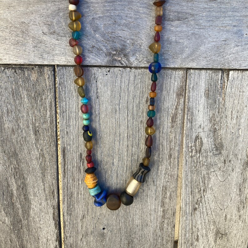 May include: A colourful beaded necklace with a variety of glass and wooden beads. The necklace features a mix of blue, red, brown, and yellow beads.
