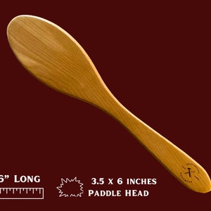May include: A 16-inch long wooden paddle with a 3.5 x 6 inch paddle head. The paddle is made of light brown wood and has a smooth finish. The paddle head is slightly rounded and has a small, dark brown logo on the bottom.