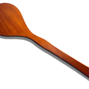 Puede incluir: Una cuchara de cocina de madera con una cabeza ancha y redondeada y un mango largo y curvado. La cuchara está hecha de madera de color marrón rojizo cálido y tiene un pequeño agujero en el extremo del mango para colgarla. La cuchara está diseñada para remover y servir alimentos.