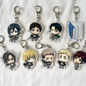 May include: A selection of acrylic keyrings featuring characters from the anime series "Attack on Titan." Each keyring displays a different character in a chibi style, with silver key rings. The keyrings are clear with colourful character designs.