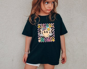 May include: A black t-shirt with a colourful graphic print featuring a smiley face with wings and the text "A Little Bit Dramatic".