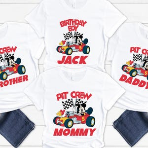 May include: White t-shirts with a cartoon race car design featuring Mickey Mouse. The shirts have text that reads "Pit Crew Brother", "Birthday Boy Jack", "Pit Crew Daddy", and "Pit Crew Mommy" in red. The shirts are paired with blue jeans.