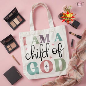 May include: A white tote bag with the text "I AM A child of GOD" in colorful letters. The bag is surrounded by makeup, including eyeshadow palettes, brushes, and a lipstick, all arranged on a pink surface.