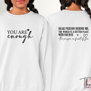 Pu&ograve; includere: Felpa bianca con la scritta "YOU ARE enough" sul davanti e "DEAR PERSON BEHIND ME, THE WORLD IS A BETTER PLACE WITH YOU IN IT. -the person in front of you" sul retro. Scritta nera e dettagli a cuore.