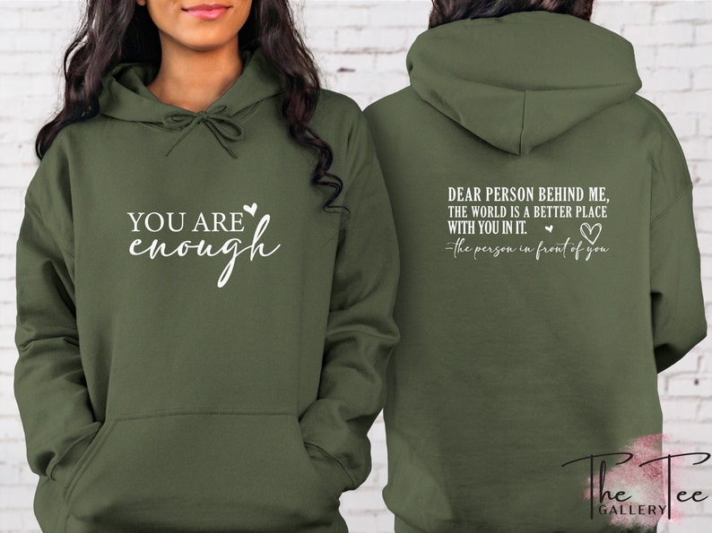Pu&ograve; includere: Felpa con cappuccio verde oliva con la scritta "YOU ARE enough" sul davanti. Il retro della felpa ha la scritta "DEAR PERSON BEHIND ME, THE WORLD IS A BETTER PLACE WITH YOU IN IT." e "-the person in front of you."