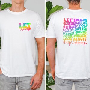 May include: White t-shirt with a rainbow graphic that says "Let them" on the front and "Let them misunderstand you, judge you, gossip about you, never doubt your worth, your beauty, Keep Shining" on the back.
