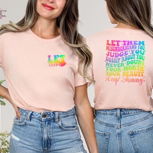May include: Pink t-shirt with a rainbow graphic that says "Let them" on the front and "Let them misunderstand you, judge you, gossip about you, never doubt your worth, your beauty, Keep Shining" on the back.