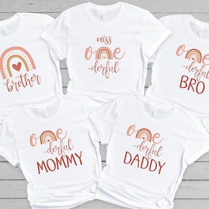 May include: Five white t-shirts with a rainbow design and the text "one-derful" with different words underneath. The shirts say "miss one-derful", "one-derful BRO", "one-derful MOMMY", "one-derful DADDY", and "brother".
