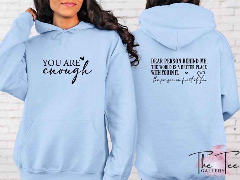 Pu&ograve; includere: Felpa con cappuccio azzurra con la scritta "YOU ARE enough" sul davanti. Il retro della felpa ha la scritta "DEAR PERSON BEHIND ME, THE WORLD IS A BETTER PLACE WITH YOU IN IT." con un simbolo a forma di cuore. Il logo The Tee Gallery &egrave; in basso.