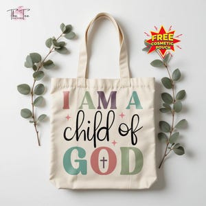 May include: Cream-colored tote bag with the text "I AM A child of GOD" in various colors. The bag has a simple design with a cross symbol in the word "GOD". The bag has two handles and is decorated with sprigs of greenery.