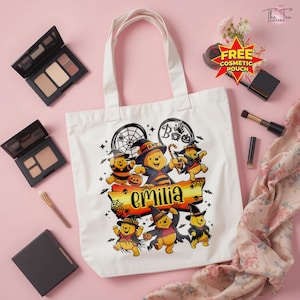 May include: A white canvas tote bag featuring a graphic of multiple cartoon bears dressed in Halloween costumes, including witch hats and capes, surrounding a banner with the name Emilia printed in black text, with spiderwebs and stars.
