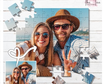 May include: A personalized jigsaw puzzle featuring a couple wearing sunglasses and hats, posing for a photo. The puzzle is partially assembled, with some pieces scattered around. The image is set against a white wooden background. The Tee Gallery logo is in the top right corner.