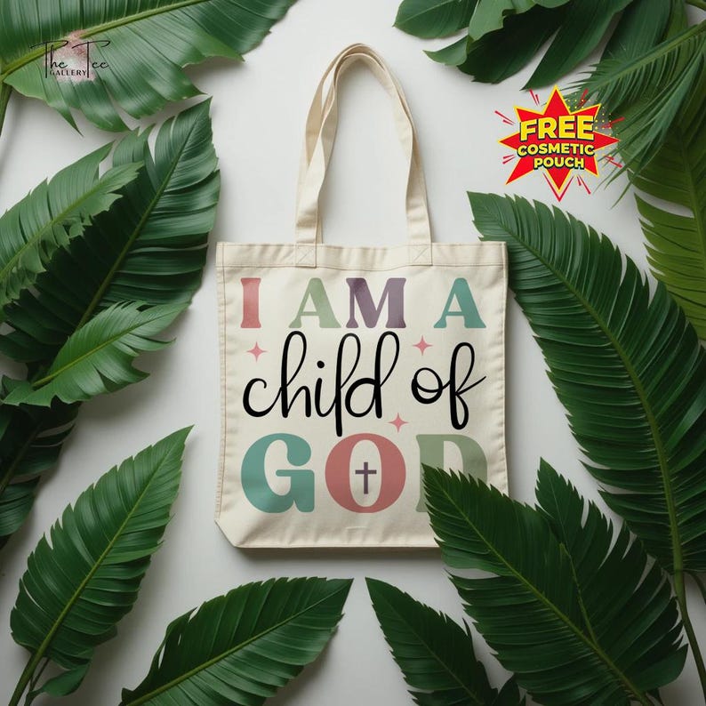 May include: Cream-colored tote bag with the text "I AM A child of GOD" in various colors. The bag has a cross symbol in the letter "O". The bag has cream-colored handles. The bag is surrounded by green leaves.