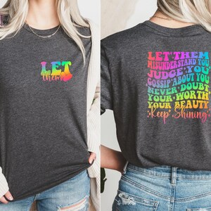 May include: A dark heather grey t-shirt with a rainbow graphic that says "Let them" on the front and "Let them misunderstand you, judge you, gossip about you, never doubt your worth, your beauty, keep shining" on the back.