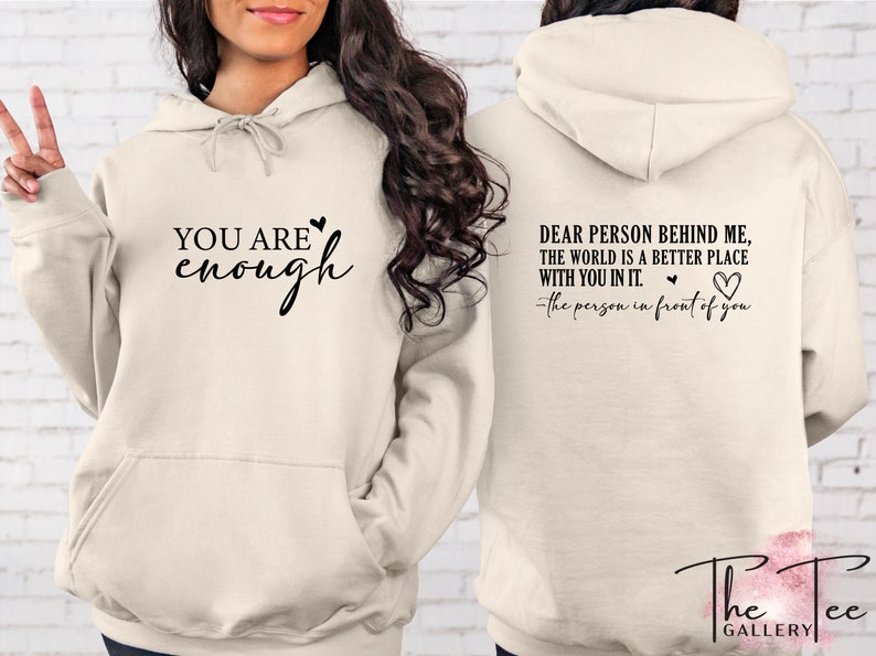 Pu&ograve; includere: Felpa con cappuccio color crema con la scritta "YOU ARE enough" sul davanti e "DEAR PERSON BEHIND ME, THE WORLD IS A BETTER PLACE WITH YOU IN IT. -the person in front of you" sul retro. Presenta una tasca frontale e un cappuccio con coulisse.