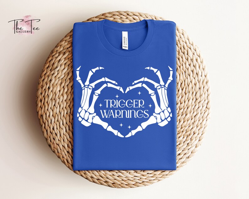 May include: A royal blue t-shirt with a white skeleton hand design making a heart shape. The text "TRIGGER WARNINGS" is inside the heart.