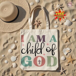 May include: Cream-colored tote bag with the text "I AM A child of GOD" in various colors. The bag is on a sandy surface with a straw hat, seashells, and starfish.